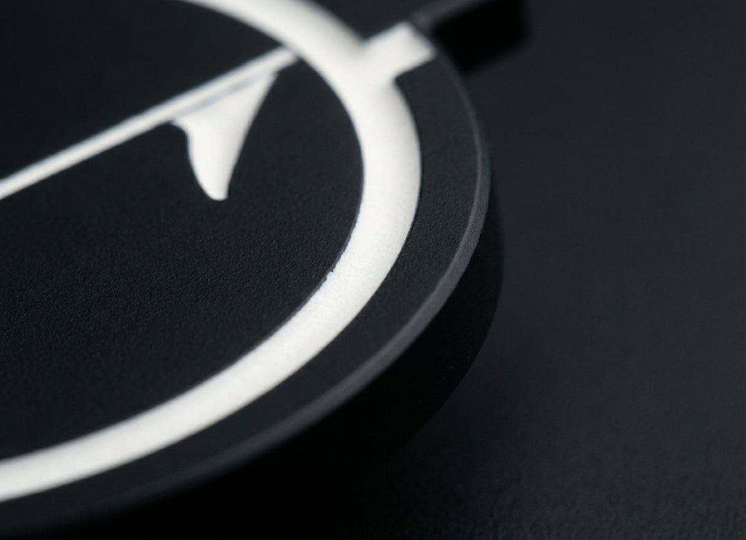 Close-up of matte black golf ball marker edge showing thickness and embedded white inlay