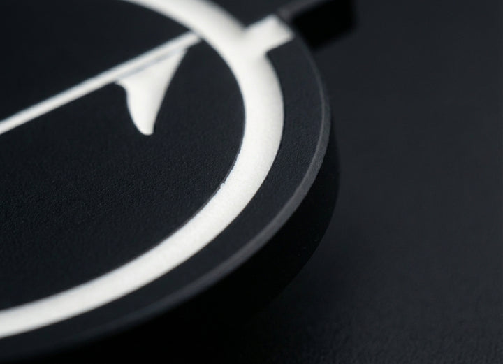 Close-up of matte black golf ball marker edge showing thickness and embedded white inlay