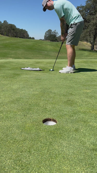 A photograph of the magnetic golf towel on a golf course, with a golf ball next to the towel.